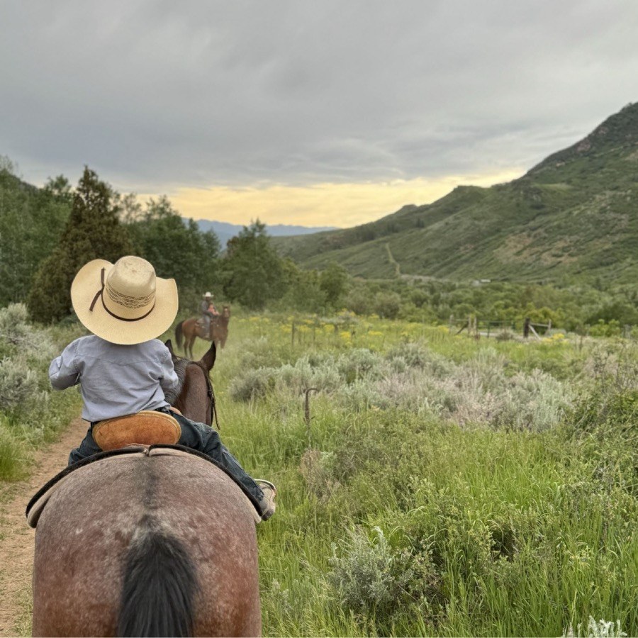 Young rider on horseback heading into Utah mountain valley at L2 Ranch